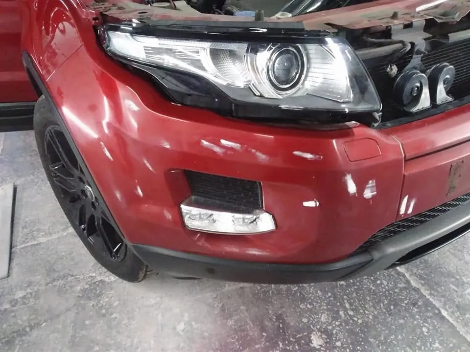 The front corner of a red car, its bumper scraped and scuffed down to white marks