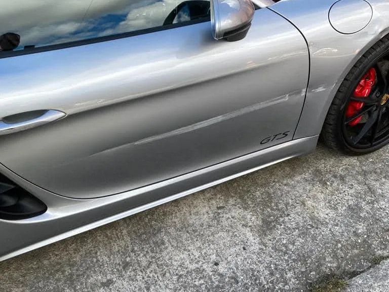 The side of a silver Porsche Boxster, a long scrape along its door and marks on the front wing